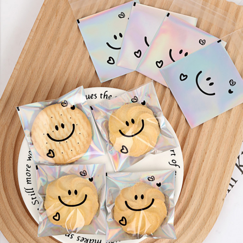Bolsa de embalaje de galletas crujiente de copo de nieve de 100 piezas, bolsa autoadhesiva con cara sonriente, bolsa transparente con láser para galletas