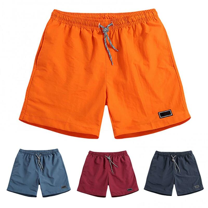 Celana olahraga pria, celana pantai kasual bersirkulasi cepat kering bersaku warna Solid latihan pantai