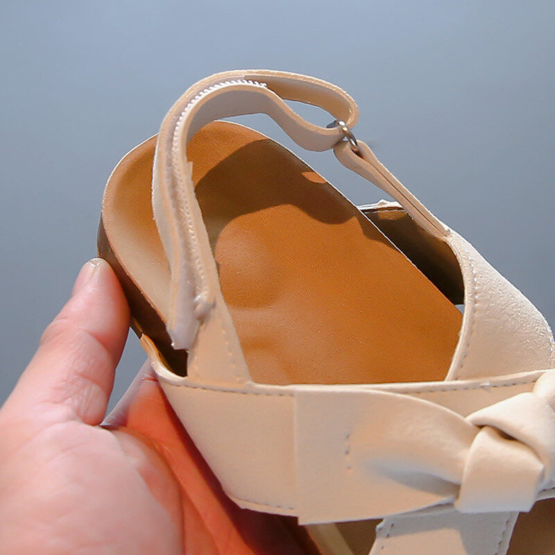 รองเท้าแตะโบว์สีทึบสำหรับเด็กผู้หญิงรองเท้าส้นเตี้ยมีห่วงทำจากหนัง PU พื้นนิ่มแฟชั่นรองเท้าแตะไม้ก๊อกสำหรับเด็กรองเท้าแตะชายหาด
